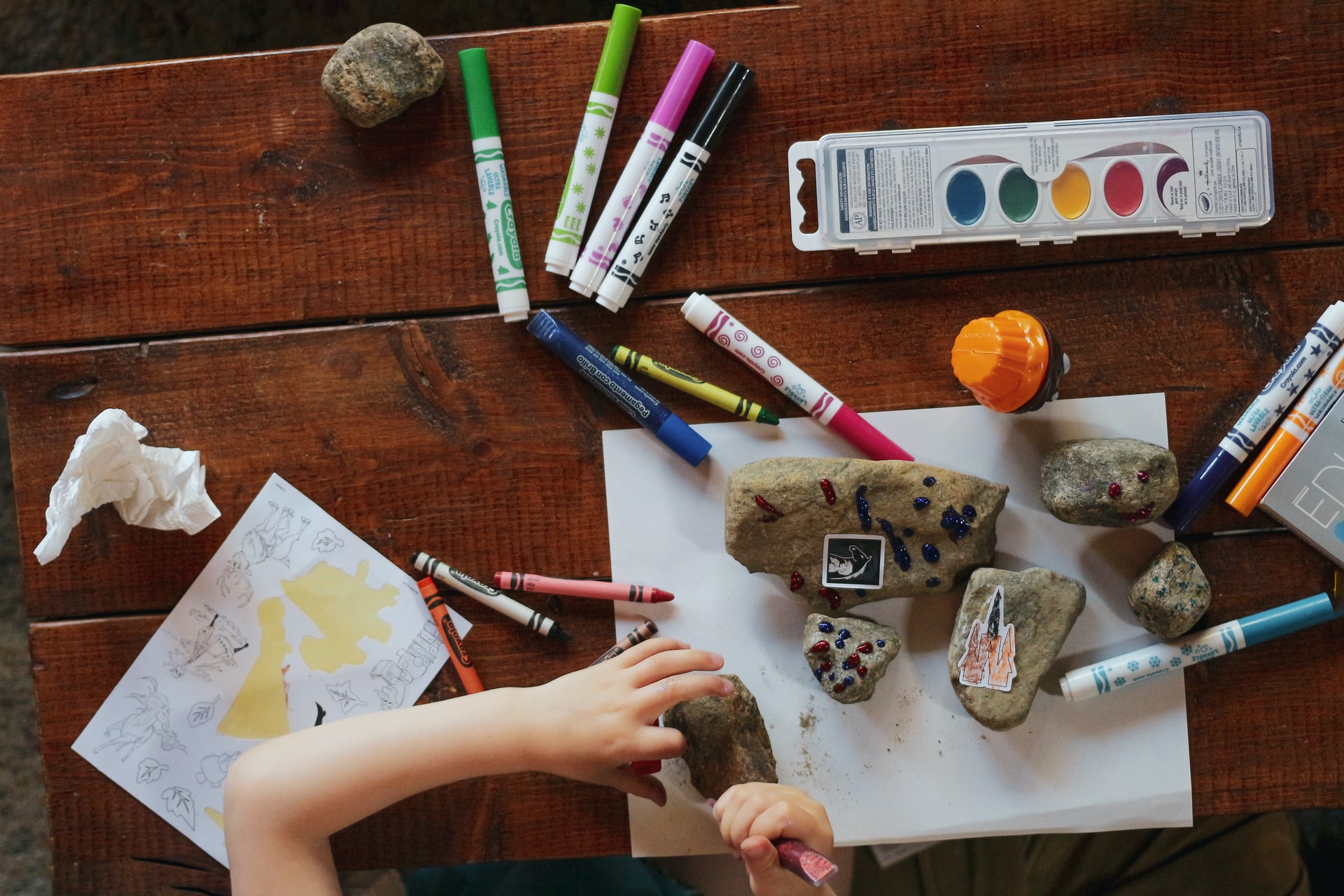 enfant sur une table avec des crayons peinture et cailloux